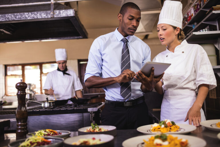 Male manager and female chef using digital tablet in kitchen at hotel