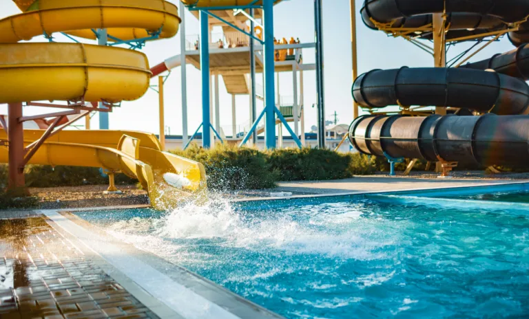 An woman an descended from a large, high yellow slide into a pool of clear, clear water and created more spray
