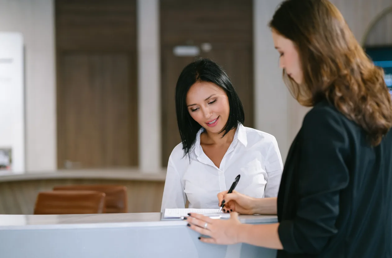 Portrait of friendly young woman reception standing behind the reception at desk of hotel with customer visitor check-out process in hotel