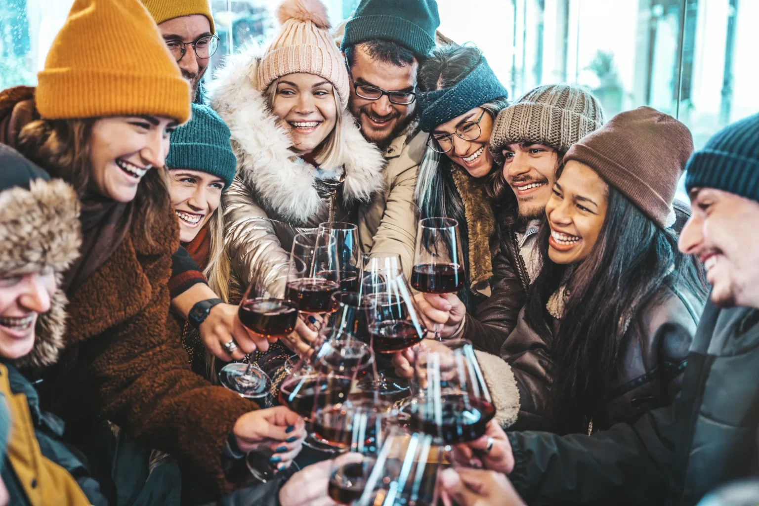 Happy multiracial friends toasting red wine at restaurant terrace - Group of young people wearing winter clothes having fun at outdoors winebar table - Dining life style and friendship concept. resort procurement services