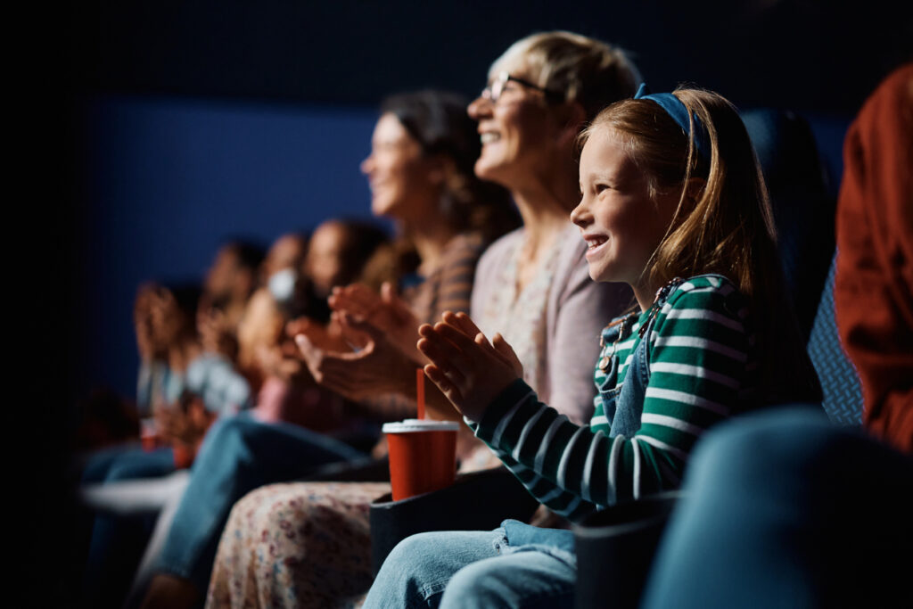 Happy little girl and her grandmother applauding while watching a movie in cinema. concessions procurement