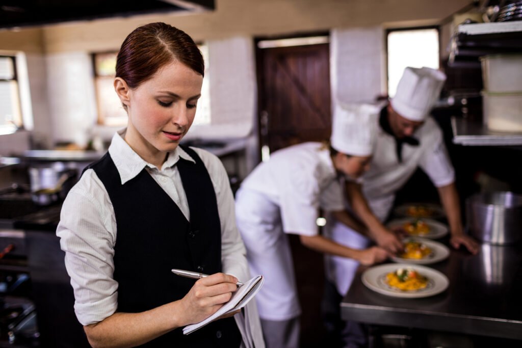 Female waitress noting an order on notepad in kitchen at hotel