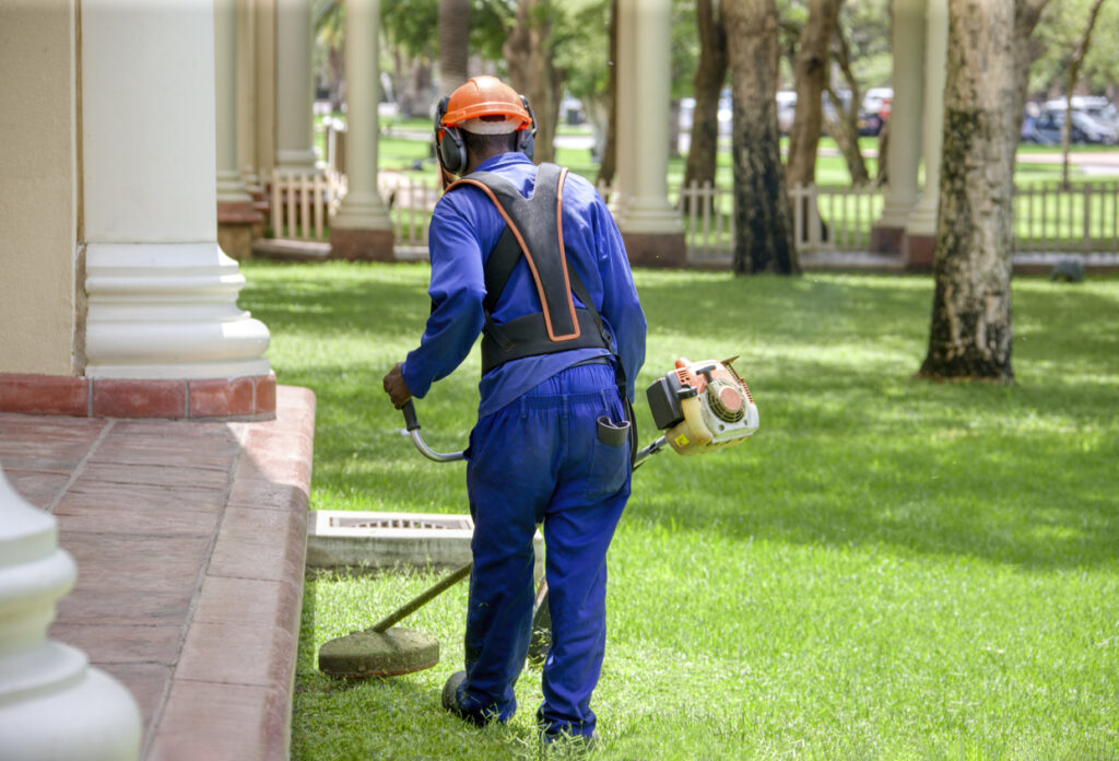 african man , contractor, with a trimmer cutting grass on the meadow in front of the hotel