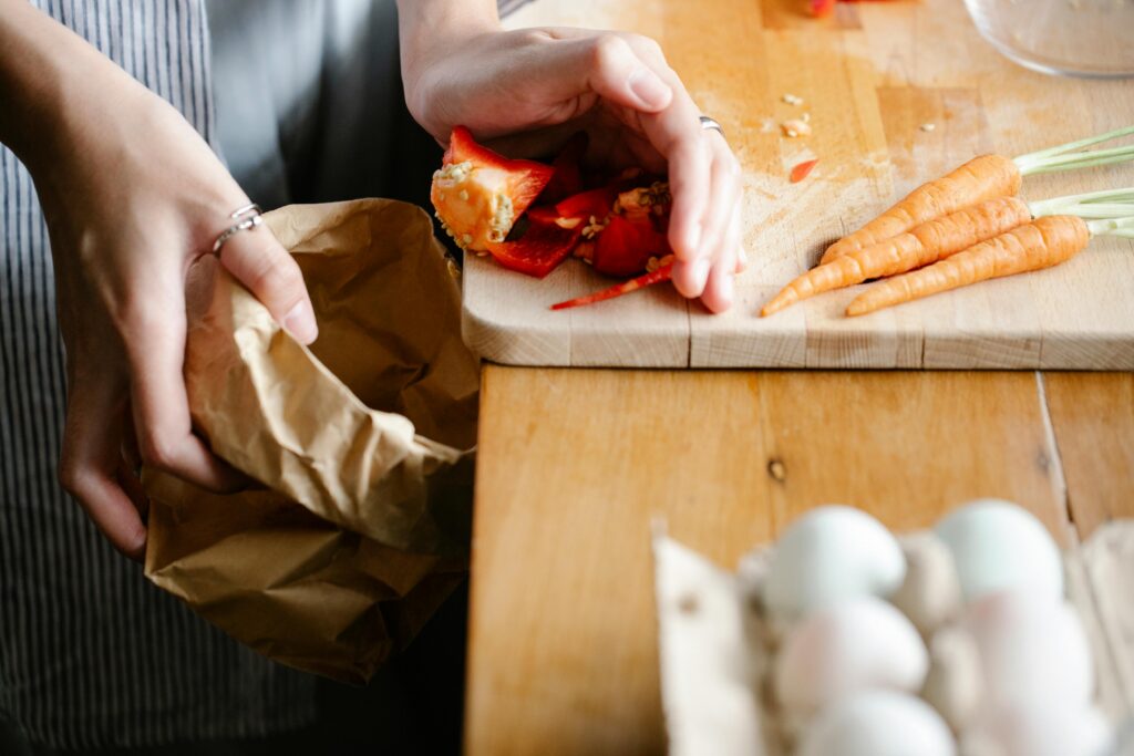 Kitchen worker discarding vegetable scraps during food prep, illustrating ways to reduce food waste in hospitality operations