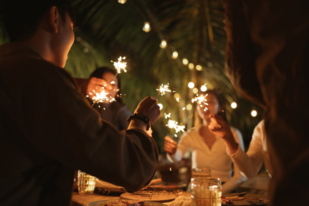 Selective focus hand. People holding firework sparklers having fun with friends group in new year festival celebrating at night party outdoor. Friendship and new year celebration concept.