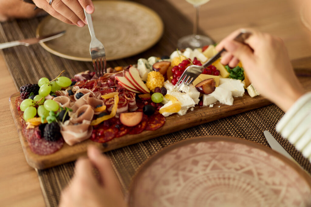 A close-up of hands enjoying a sharing platter with cheese, meats, and fruits.